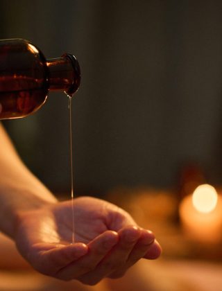 Medium close up of unrecognizable female hand holding jar and pouring essential oil into palm